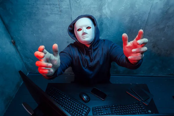 Hacker anónimo con máscara facial que trabaja en la computadora en la habitación oscura —  Fotos de Stock