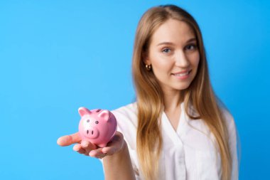 Mavi arka planda kumbarası olan güzel, gülümseyen genç bir kadın.