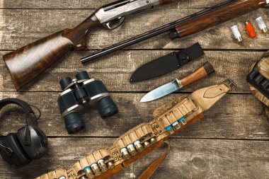 Tüfek, bıçak, dürbün ve fişekler de dahil olmak üzere eski ahşap arka planda avlanma ekipmanları.