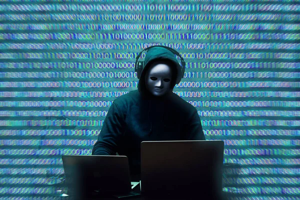 Hacker anónimo con máscara facial que trabaja en la computadora en la habitación oscura — Foto de Stock