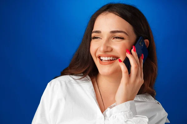 Jeune femme brune parlant au téléphone sur fond bleu — Photo