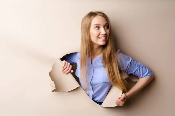 Hermosa mujer joven mirando a través de un agujero en papel beige — Foto de Stock