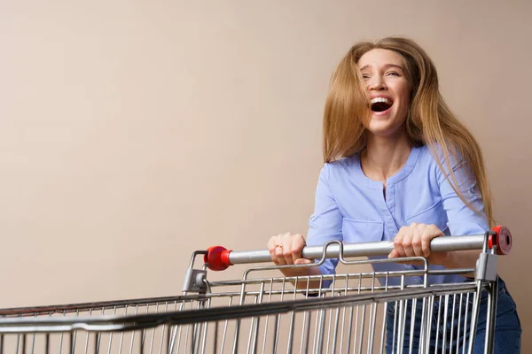 Jonge vrolijke vrouw met lege winkelwagen op beige achtergrond — Stockfoto