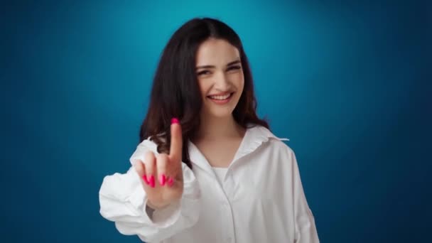 Χαμογελαστή νεαρή γυναίκα δείχνει στάση χειρονομία σε μπλε φόντο — Αρχείο Βίντεο