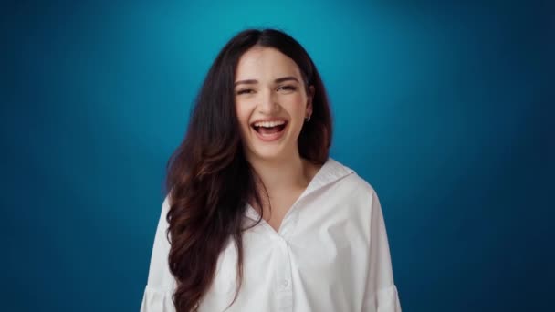 Fröhliche junge Frau lächelt und lacht vor blauem Hintergrund — Stockvideo
