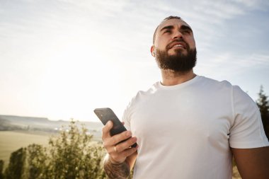 Kırsalda yürürken cep telefonu kullanan genç bir erkek.