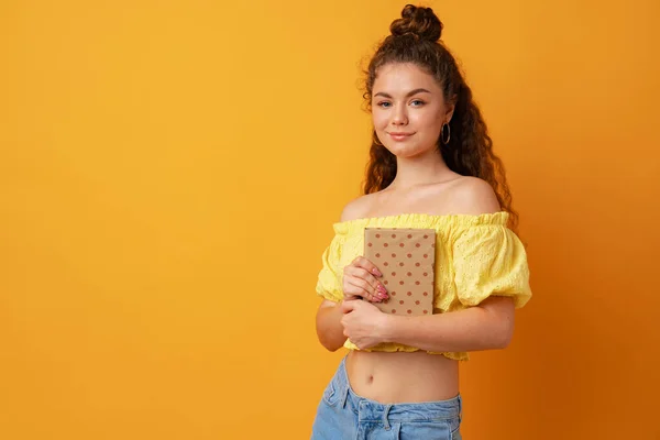Mladá kudrnatá žena student drží knihu na žlutém pozadí — Stock fotografie