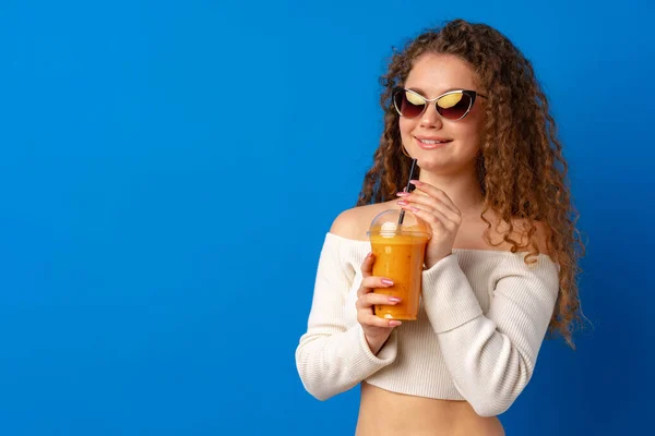 Όμορφη σγουρά μαλλιά γυναίκα πίνοντας χυμό πορτοκάλι σε μπλε φόντο — Φωτογραφία Αρχείου