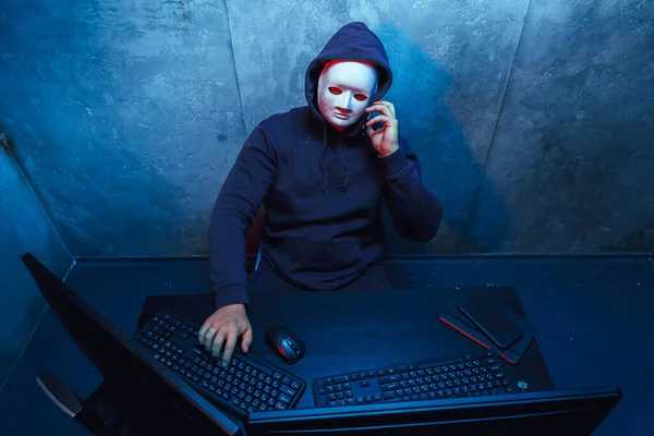 Hacker anonimo con maschera facciale che lavora al computer in camera oscura — Foto Stock