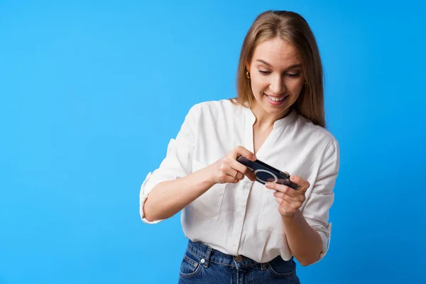 Positive junge Frau spielt Spiele auf Smartphone vor blauem Hintergrund — Stockfoto