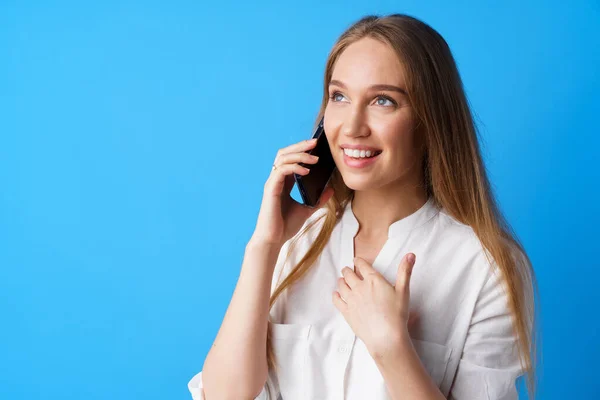 Feliz sorrindo jovem mulher falando ao telefone contra fundo azul — Fotografia de Stock