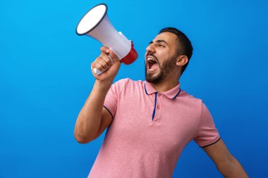 Megafonlu genç Arap adam mavi arka planda izole edilmiş bir şey ilan ediyor.