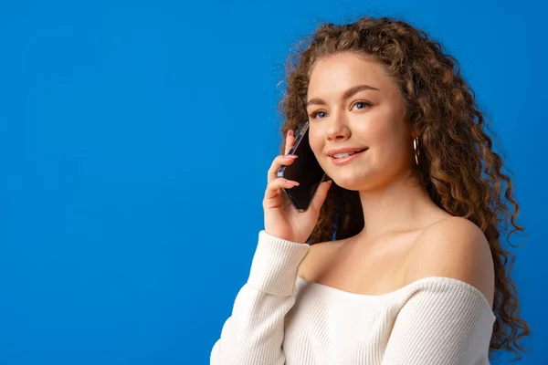 Joven mujer rizada hablando por teléfono contra fondo azul — Foto de Stock