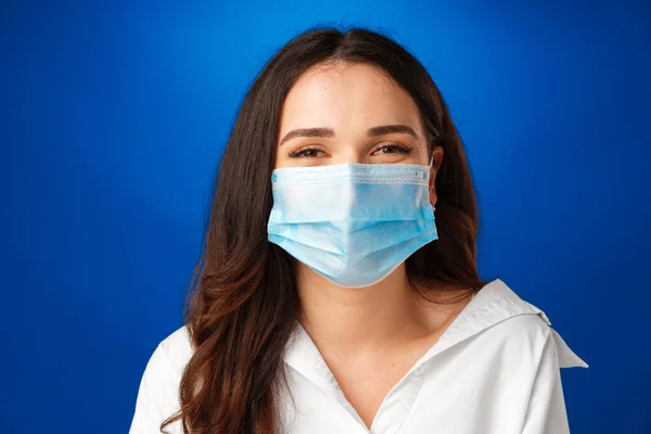 Молодая красивая брюнетка носит медицинскую маску на синем фоне — стоковое фото