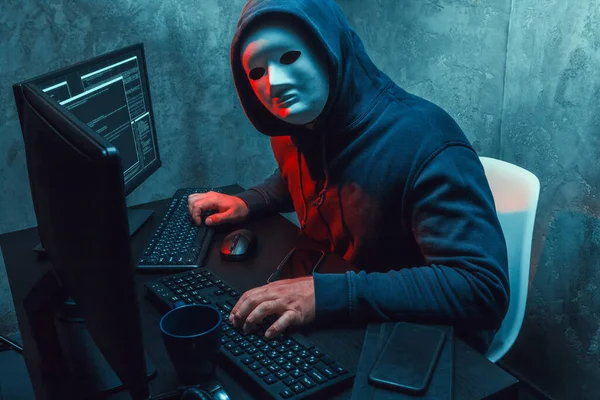 Yüz maskesi takan anonim hacker karanlık odada bilgisayarla çalışıyor. — Stok fotoğraf