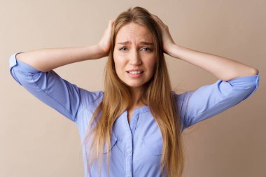 Gergin ve kafası karışmış genç bir kadın başını bej arka planda tutuyor.