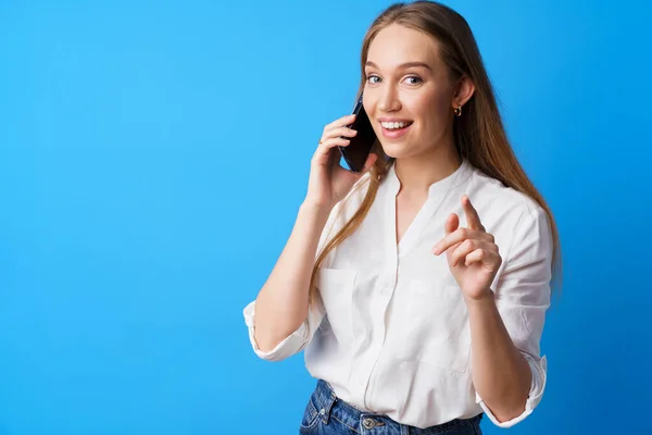 Boldog mosolygós fiatal nő beszél a telefonon a kék háttér — Stock Fotó