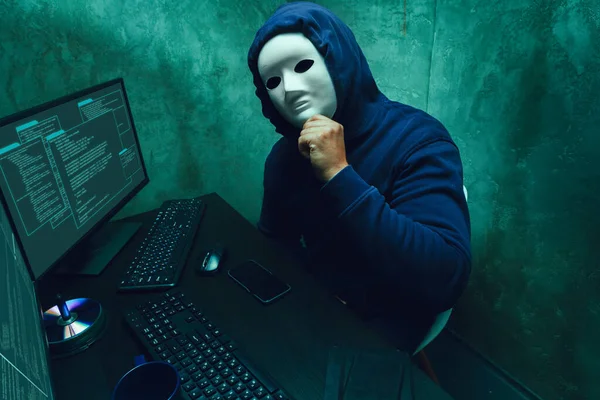 Hacker anónimo con máscara facial que trabaja en la computadora en la habitación oscura — Foto de Stock