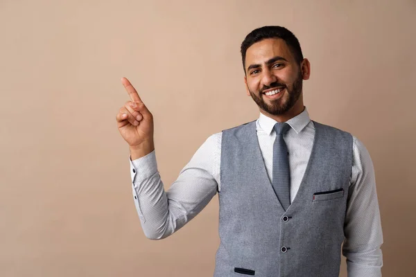 Ung stilig arabisk man över beige bakgrund pekar på kopiera utrymme och leende — Stockfoto