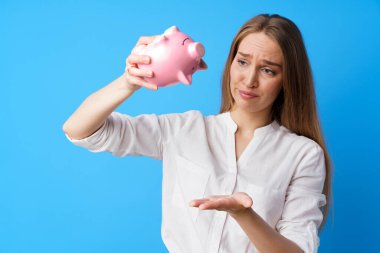 Mutsuz bir kadın kumbarasını mavi arka planda tutuyor.