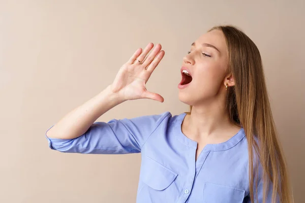 Mujer rubia joven gritando algo fuerte, haciendo anuncio, sobre fondo beige — Foto de Stock