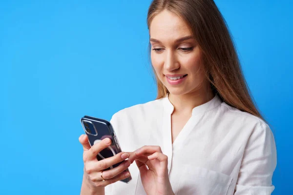 Close up de jovem loira usando seu smartphone contra fundo azul — Fotografia de Stock