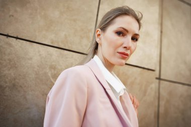 Kotlu ve beyaz pamuklu bluzlu şık kız gri duvarın yanında poz veriyor.