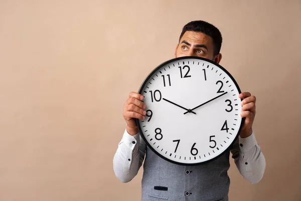 Hombre árabe joven sosteniendo gran reloj de pared en la mano sobre fondo beige — Foto de Stock