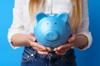 Dişi eller domuz kumbarasını mavi arka planda tutuyor