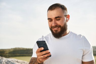 Kırsalda yürürken cep telefonu kullanan genç bir erkek.