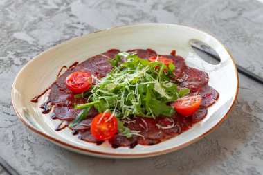 Gri yüzeyde roka ve parmesanlı biftek carpaccio.