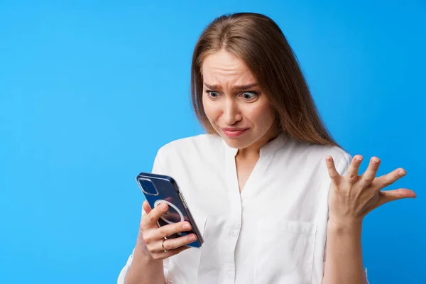 젊은 분노 한 여성 이 핸드폰을 사용하고 있는 모습, 누군가에게 문자를 보내는 것, 파란 배경 — 스톡 사진