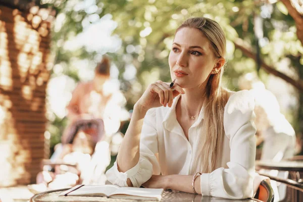 Pensive jonge zakenvrouw zitten in outdoor cafe en het maken van notities — Stockfoto