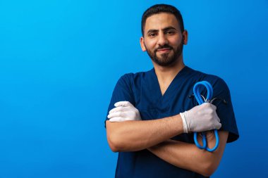 Mavi üniformalı yakışıklı erkek doktor. Steteskopu mavi arka planda.