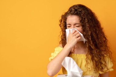 Sarı arka planda mendil tutan hasta genç bir kadın.