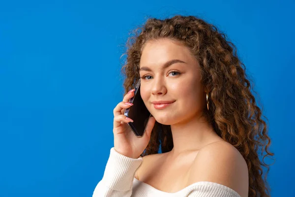 Genç kıvırcık kadın telefonda mavi arka planda konuşuyor. — Stok fotoğraf