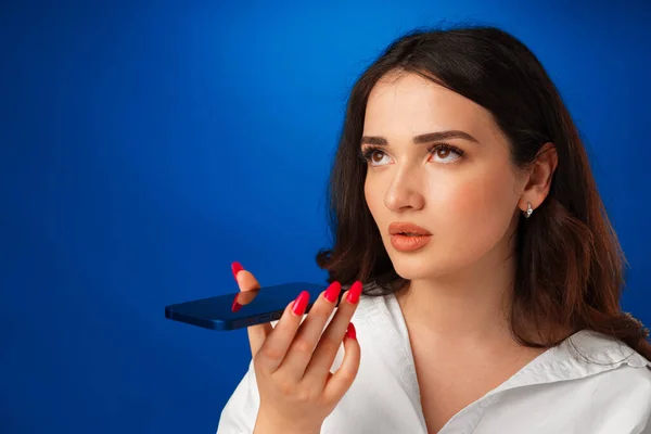 Jovem morena falando ao telefone contra fundo azul — Fotografia de Stock