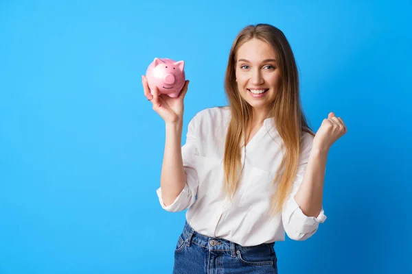 Krásná usmívající se mladá žena s prasátko banka na modrém pozadí — Stock fotografie