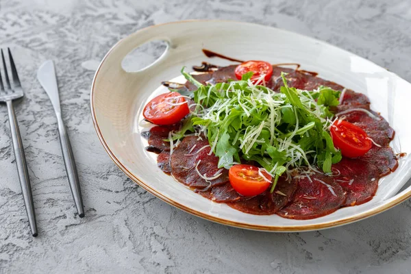 Gri yüzeyde roka ve parmesanlı biftek carpaccio.