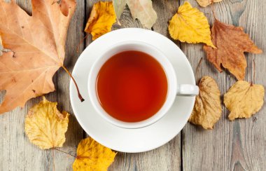 Bir fincan çay ve sonbahar yaprakları masada.