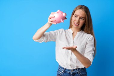Mutsuz bir kadın kumbarasını mavi arka planda tutuyor.