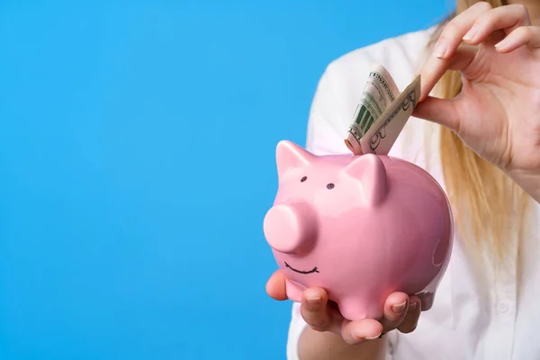 Feminino colocando dinheiro em rosa porquinho banco contra fundo azul — Fotografia de Stock