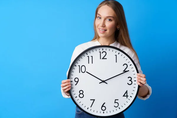 Atractiva joven mujer sosteniendo gran reloj de pared contra fondo azul — Foto de Stock