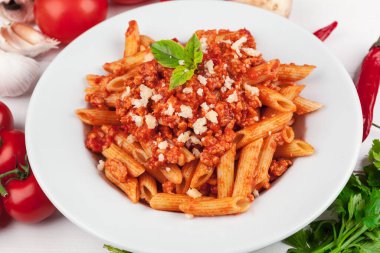 Etli makarna, domates sosu ve sebzeler masada.