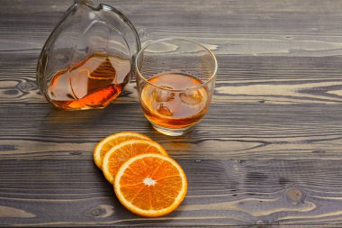 Koyu ahşap arka planda portakal meyveli viski bardağı.