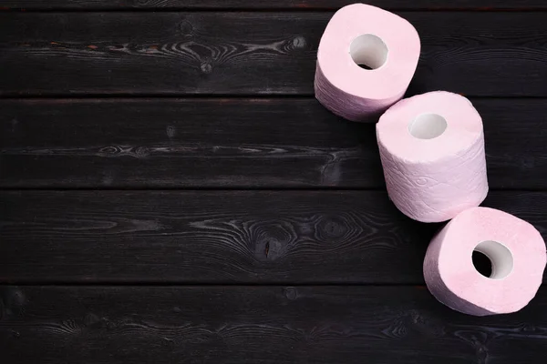 Rollos de papel higiénico rosa pastel sobre fondo de madera negro — Foto de Stock