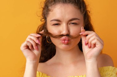 Sarı arka planda saçları olan genç bir kadın bıyık yapıyor.