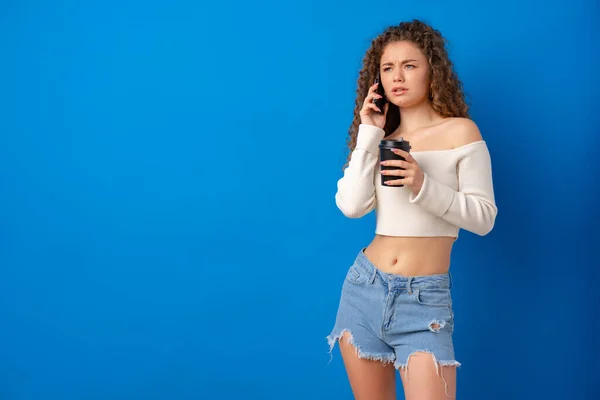 Junge lockige Frau telefoniert vor blauem Hintergrund — Stockfoto