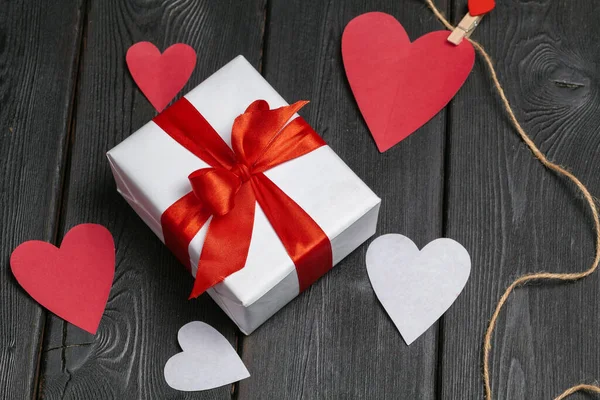 Dárková krabička s červenou mašlí a papírových srdcí na dřevěném pozadí pro Valentýna — Stock fotografie