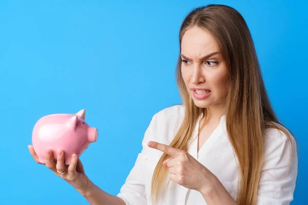 Mujer infeliz sosteniendo alcancía moneybox contra fondo azul — Foto de Stock